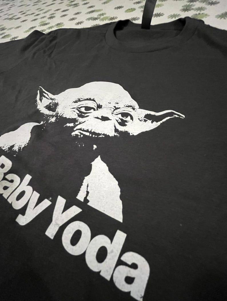 May include: Black t-shirt with a white graphic of Baby Yoda. The text "Baby Yoda" is printed in white below the image.