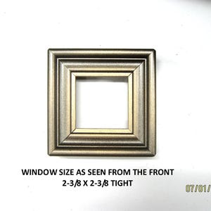 May include: A square, metallic gold-toned frame with a stepped, beveled profile. Text below reads: WINDOW SIZE AS SEEN FROM THE FRONT 2-3/8 X 2-3/8 TIGHT. The frame features a hollow center and a smooth, reflective finish on its edges.