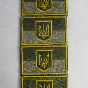 Könnte beinhalten: Vier gestickte Aufnäher mit der ukrainischen Flagge. Jeder Aufnäher ist rechteckig und hat einen gelben Umriss. Die Flagge ist ein horizontaler Dreifarbensatz aus Blau, Gelb und Blau. Das gelbe Band zeigt einen goldenen Dreizack.
