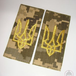 May include: Two military-style shoulder patches with a yellow embroidered Ukrainian trident on a camouflage background.