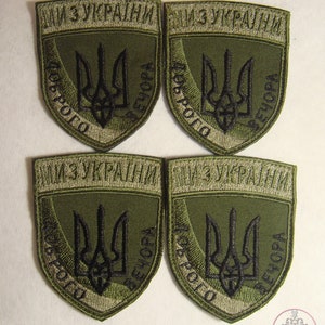 Könnte beinhalten: Vier grüne gestickte Aufnäher mit dem ukrainischen Wappen und dem Text "МИ З УКРАЇНИ" (Wir sind mit der Ukraine) in Schwarz.