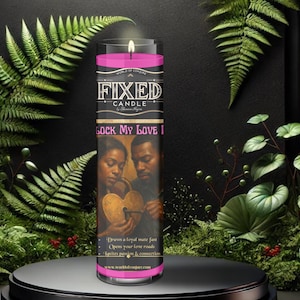 May include: A cylindrical glass candle with pink wax, featuring a label with the text FIXED CANDLE and LOCK MY LOVE. The label displays an illustration of two people holding a heart-shaped padlock. The candle has a lit wick at the top.