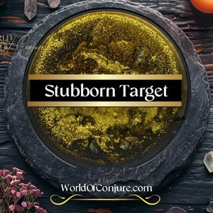 May include: A black slate plate with a gold glitter filled circle in the center. The circle has a black and gold banner across the center that reads "Stubborn Target". The plate is on a dark wood surface with crystals and other decorative items.