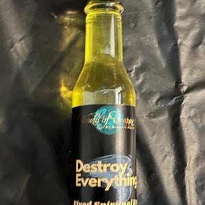 May include: A clear glass bottle filled with yellow liquid, topped with a black cap. The black label features the text World of Conjure by Shandon Hayes, Destroy Everything, and Fixed Spiritual Bath, with a graphic of a swirling tornado.