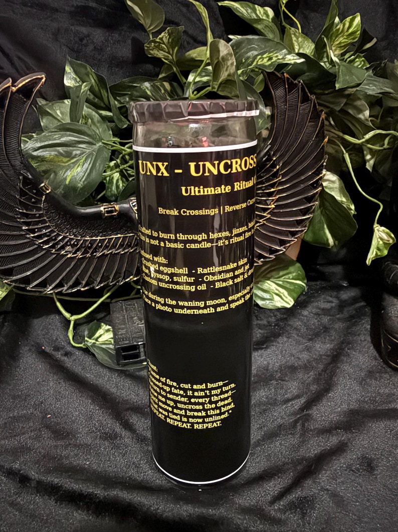 K&ouml;nnte beinhalten: Eine hohe, zylindrische schwarze Kerze in einem Glasbeh&auml;lter mit einem Etikett, das den gelben Text UNX - UNCROSS Ultimate Ritual tr&auml;gt. Das Etikett enth&auml;lt Anweisungen und Zutatenlisten vor einem dunklen Hintergrund mit schwarzen Fl&uuml;geln.