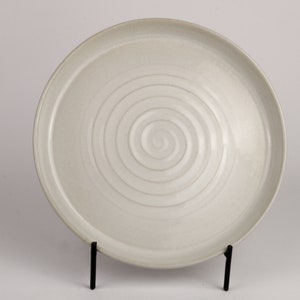 May include: A white ceramic plate with a spiral design. The plate is on a black stand.