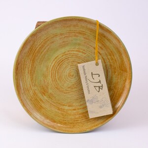 Pode incluir: Um prato de cerâmica verde e marrom com um padrão de espiral. O prato é feito à mão e tem uma etiqueta que diz "LJB Handmade Pottery & Ceramics".