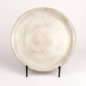 May include: A white ceramic plate with a swirl design. The plate is on a black metal stand.