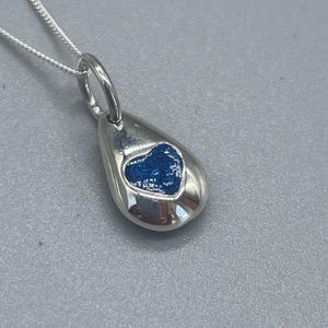 K&ouml;nnte beinhalten: Eine silberne Tropfen-Halskette mit einem blauen Herz-Anh&auml;nger.