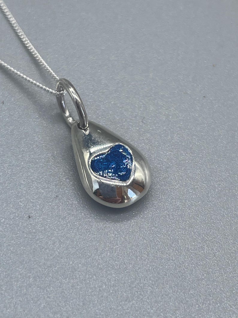 K&ouml;nnte beinhalten: Eine silberne Tropfen-Halskette mit einem blauen Herz-Anh&auml;nger.