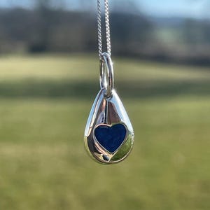 K&ouml;nnte beinhalten: Eine silberne Tropfen-Anh&auml;ngerkette mit einem blauen Herz-Ausschnitt. Der Anh&auml;nger h&auml;ngt an einer silbernen Kette.