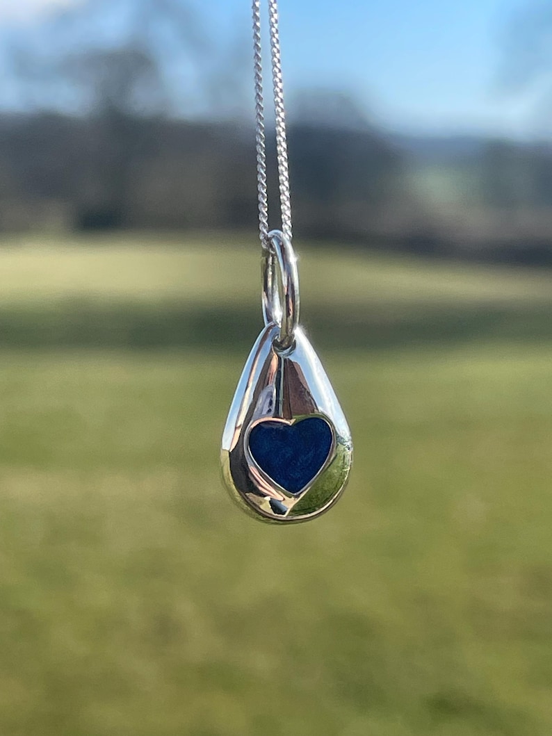 K&ouml;nnte beinhalten: Eine silberne Tropfen-Anh&auml;ngerkette mit einem blauen Herz-Ausschnitt. Der Anh&auml;nger h&auml;ngt an einer silbernen Kette.