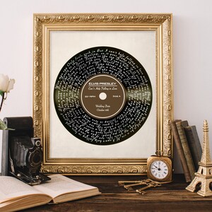Puede incluir: Una impresi&oacute;n enmarcada de un disco de vinilo negro con la letra de "Can't Help Falling in Love" de Elvis Presley impresa en blanco. La etiqueta del disco es marr&oacute;n con el t&iacute;tulo de la canci&oacute;n, el nombre del artista y la fecha de la boda "19 de octubre".