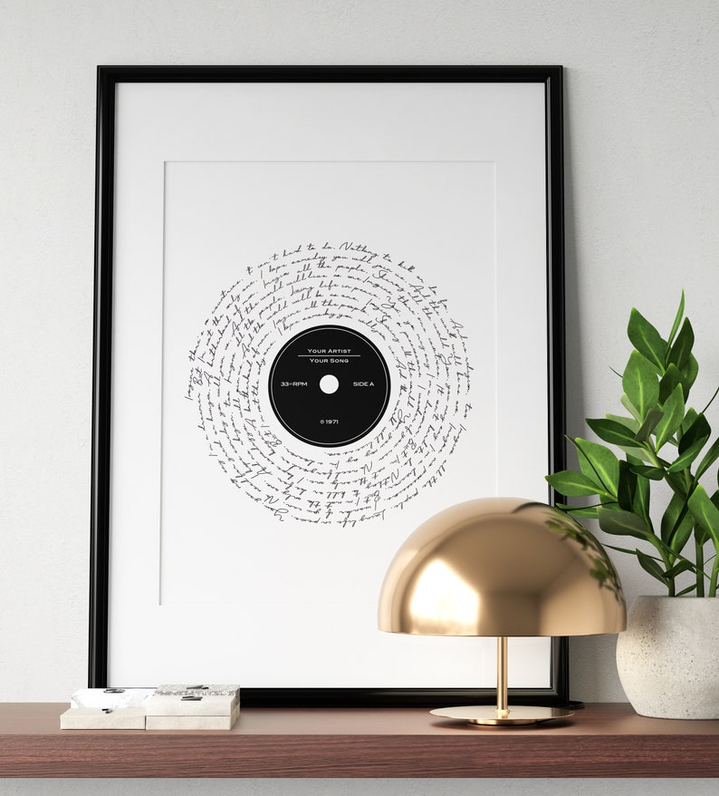 May include: A black framed print of a vinyl record with handwritten lyrics in a circular pattern. The record label says "YOUR ARTIST" and "YOUR SONG".