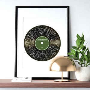 Puede incluir: Una impresi&oacute;n enmarcada de un disco de vinilo negro con la letra de la canci&oacute;n "Imagine" de John Lennon escrita en blanco en la superficie. El disco es verde y tiene el t&iacute;tulo "Imagine" y "John Lennon" escrito en &eacute;l.