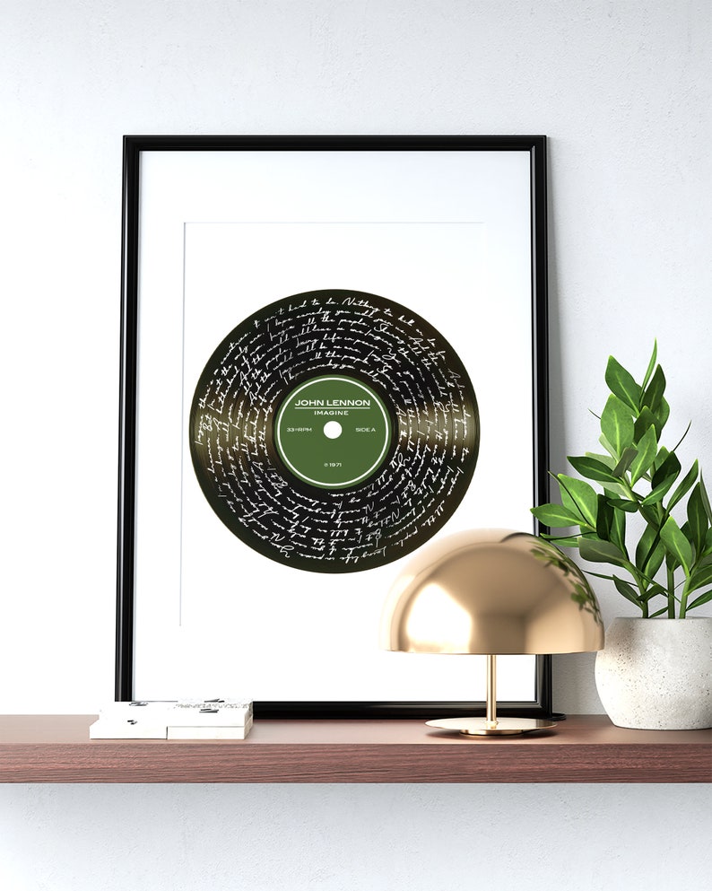 Puede incluir: Una impresi&oacute;n enmarcada de un disco de vinilo negro con la letra de la canci&oacute;n "Imagine" de John Lennon escrita en blanco en la superficie. El disco es verde y tiene el t&iacute;tulo "Imagine" y "John Lennon" escrito en &eacute;l.