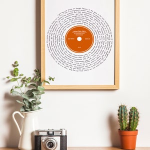 May include: A framed print of a record with the lyrics to the song "Summertime Sadness" by Lana Del Rey. The record is orange and the lyrics are written in black ink.