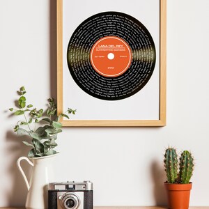 Puede incluir: Una impresi&oacute;n enmarcada de un disco de vinilo negro con el texto "Lana Del Rey Summertime Sadness 33 RPM Side A 2012" en blanco. El disco es naranja y negro con texto blanco.