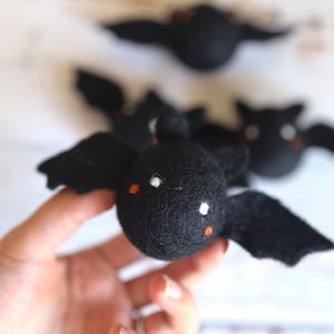 以下が含まれることがあります： 白い目とオレンジ色のアクセントが付いた黒いフェルトの蝙蝠。蝙蝠は手で持たれています。