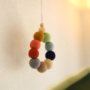 以下が含まれることがあります： 黄色、オレンジ、赤、青、緑、ベージュなど、虹色のカラーのフェルトボールガーランド。ガーランドは白い紐から吊り下げられています。
