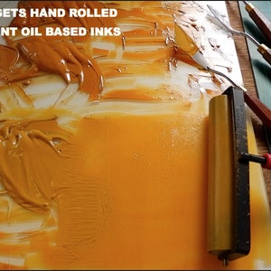 May include: A close-up of a yellow oil-based ink being spread on a white surface with a roller. The text "EVERY PRINT GETS HAND ROLLED WITH PERMANENT OIL BASED INKS" is visible at the top of the image.