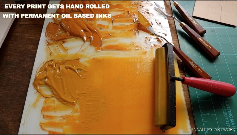 May include: A close-up of a yellow oil-based ink being spread on a white surface with a roller. The text "EVERY PRINT GETS HAND ROLLED WITH PERMANENT OIL BASED INKS" is visible at the top of the image.