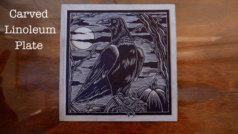 May include: A black and white linoleum block print of a raven perched on a pumpkin with a full moon in the background. The print is titled "Carved Linoleum Plate".