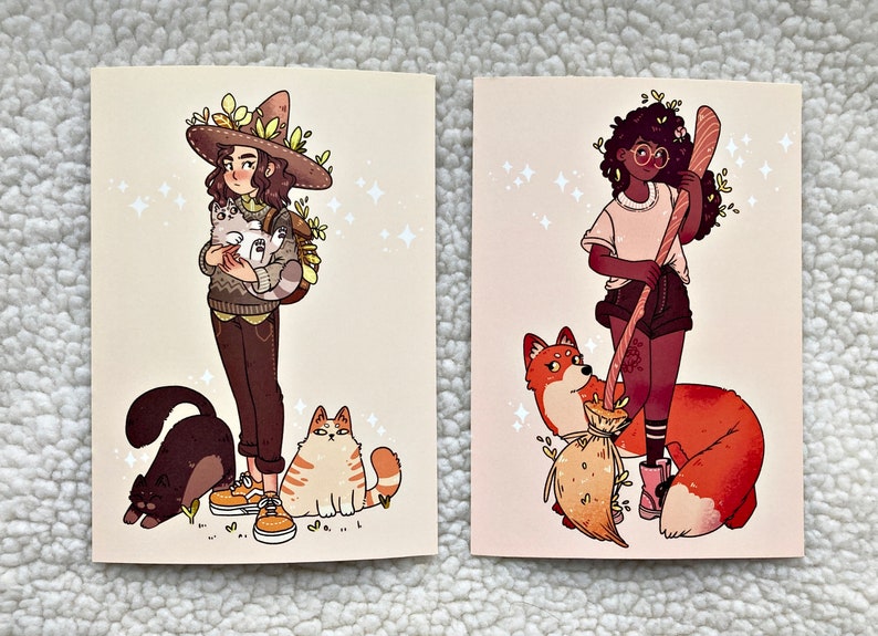 May include: Two illustrated cards featuring women with animal companions. The first card shows a woman with brown hair wearing a brown hat with green leaves and holding two white cats. She is wearing a brown sweater and brown pants. She is standing next to a black cat and a brown and white cat. The second card shows a woman with brown skin and curly black hair wearing a white shirt and black shorts. She is holding a brown broom and is standing next to a red fox.