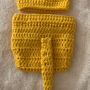 May include: A yellow crocheted lion costume for a baby, featuring a hat with brown ears and a tail with a brown tassel.
