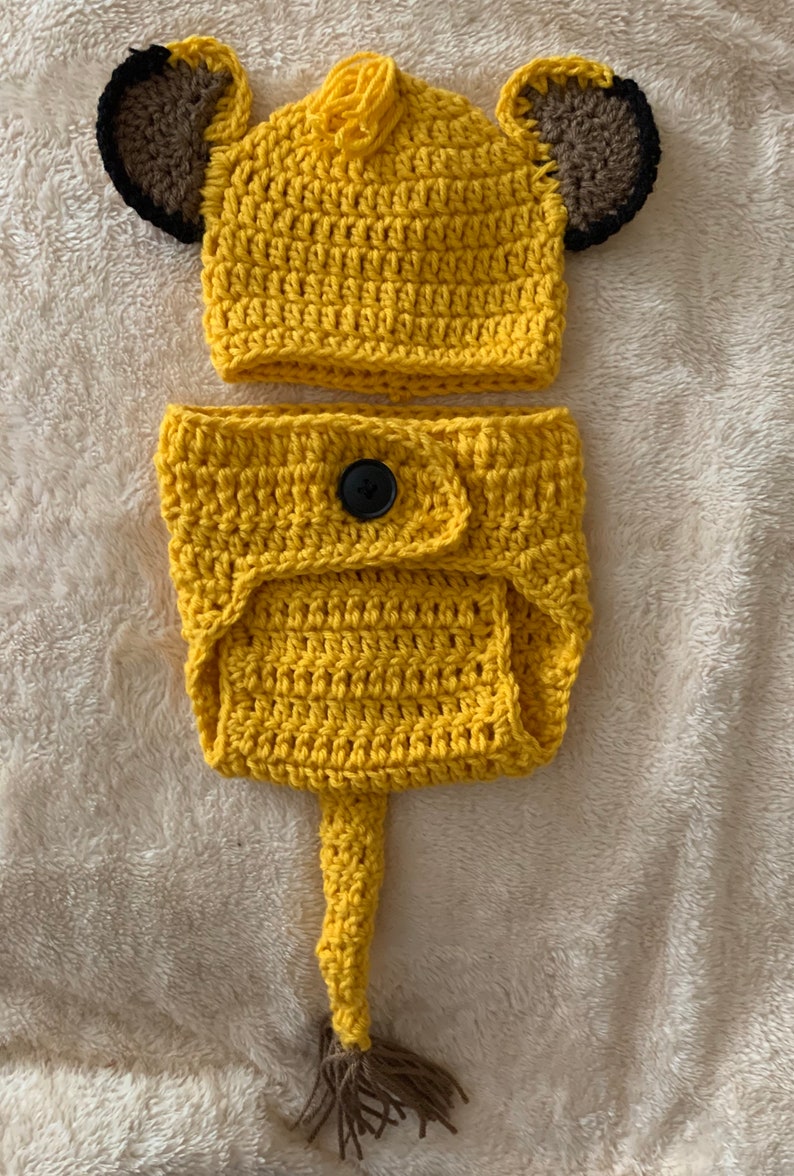 May include: A crocheted lion costume for a baby, featuring a yellow hat with brown ears and a matching yellow diaper cover with a tail.