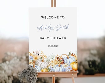 Puede incluir: Un letrero de bienvenida rectangular blanco para un baby shower sobre un caballete de madera. El letrero presenta el texto WELCOME TO, Ashley Smith, BABY SHOWER y 09.08.2024. La parte inferior está decorada con una ilustración en acuarela de calabazas azules, blancas y naranjas.