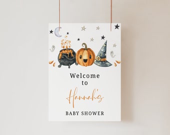 May include: A white rectangular sign featuring watercolor illustrations of a black cauldron with orange bubbles, a smiling orange pumpkin, and a dark blue witch hat. The text reads Welcome to Hannah's BABY SHOWER with stars and ghosts.