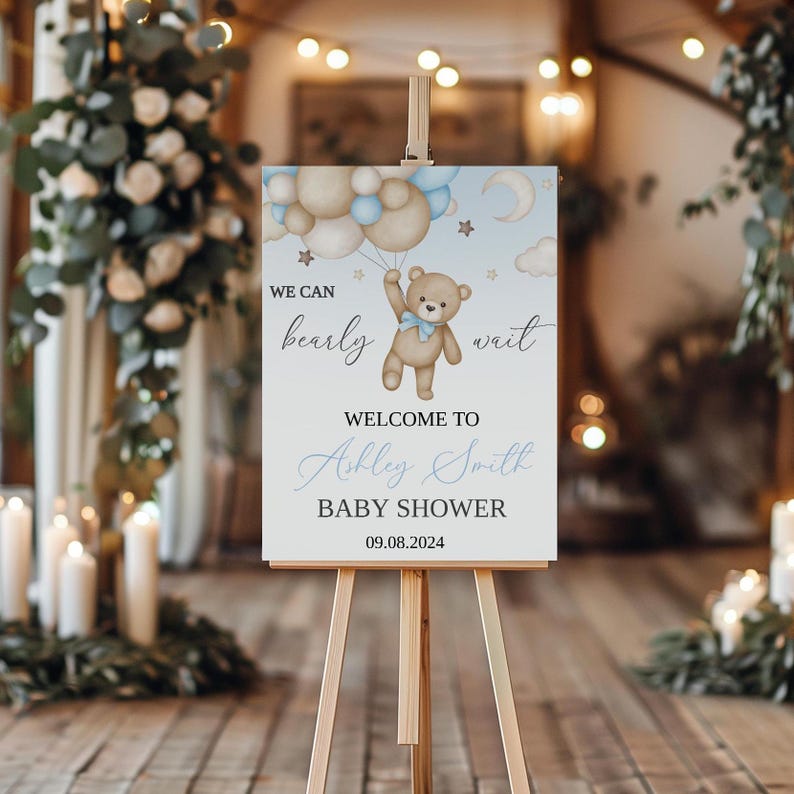 May include: A baby shower welcome sign on a wooden easel. The sign features a teddy bear holding balloons, with the text "We can bearly wait" and "Welcome to Ashley Smith Baby Shower 09.08.2024". The background includes a moon and stars.