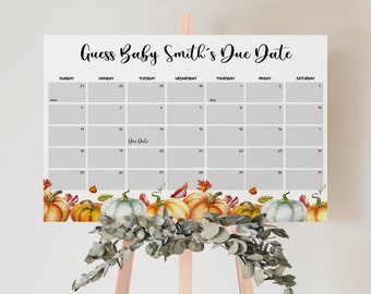 May include: A baby shower calendar with the text "Guess Baby Smith's Due Date." The calendar has a gray grid with dates and months, and a watercolor border of pumpkins and leaves. The calendar is displayed on a wooden easel.