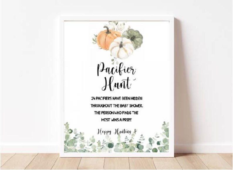 May include: White framed sign with the text "Pacifier Hunt" and details for a baby shower game. The sign features watercolor pumpkins and greenery. The sign is displayed on a wooden surface.