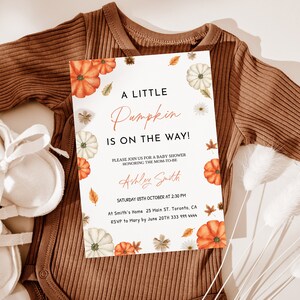 May include: A baby shower invitation with the text "A Little Pumpkin is on the Way!" features watercolor pumpkins, leaves, and daisies. The invitation is on a white background, with a brown onesie and baby booties.