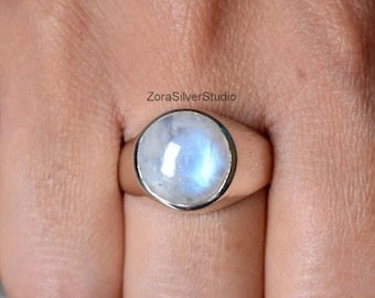 Puede incluir: Un anillo de plata con una gran piedra de luna redonda y blanca. El anillo tiene una banda simple y pulida.