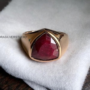 May include: A gold ring featuring a large, triangular, red ruby gemstone.