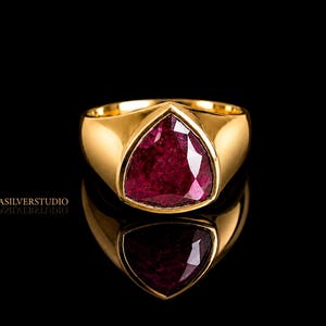 May include: A gold ring with a large, triangular, deep red gemstone. The ring is set against a black background, with a reflection of the ring visible below. The ring is from ZORASILVERSTUDIO.