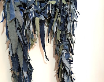 May include: A long, flowing piece of fabric made from strips of blue denim and green fabric. The fabric is frayed and has a rustic, handmade look.