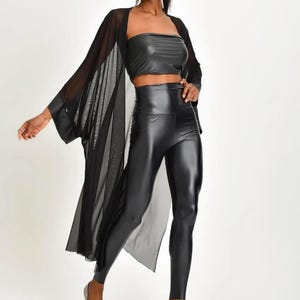 May include: A black faux leather crop top and high-waisted leggings set. A sheer black kimono-style cover-up is worn over the top. The model is wearing silver heels. The outfit is a modern, stylish ensemble.