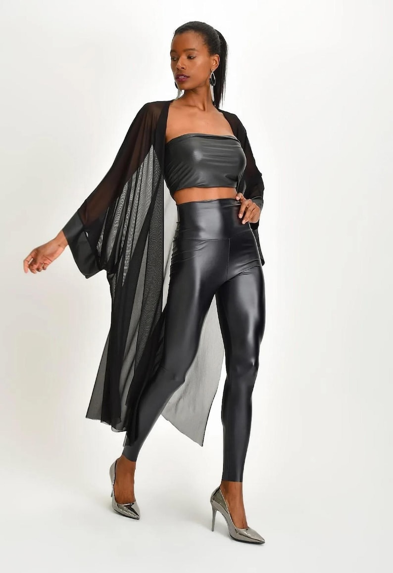 May include: A black faux leather crop top and high-waisted leggings set. A sheer black kimono-style cover-up is worn over the top. The model is wearing silver heels. The outfit is a modern, stylish ensemble.