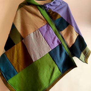 May include: A patchwork hooded poncho in a variety of colors including green, tan, purple, and blue. The poncho has a full zipper and a green hood. The design is made of rectangular fabric pieces sewn together.