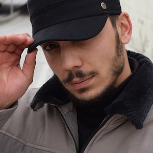 May include: A man wearing a black fleece-lined jacket with a black  military-style cap. The cap has a small metal button on the side.
