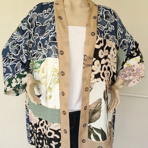 Puede incluir: Un kimono largo de patchwork azul, beige, verde, blanco y negro con un estampado floral y la palabra "CHANEL" impresa en la tela.