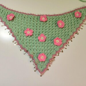 May include: A triangular crochet bandana in light mint green featuring a pink crocheted border and six small pink floral appliqu&eacute;s scattered across the surface. The edges are adorned with small, dangling metallic silver sequins.