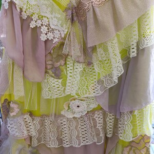 Puede incluir: Una falda de color amarillo neón brillante con múltiples capas de tela, incluyendo encaje floral blanco, volantes de gasa malva y malla. La prenda está decorada con parches florales bordados en tonos rosa, verde y blanco.
