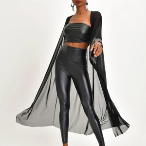 May include: A black ensemble featuring a strapless crop top, high-waisted leggings, and a sheer, flowing cape. The outfit is completed with pointed-toe heels. The clothing has a shiny, leather-like appearance.