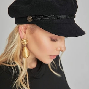 May include: A black wool cap with a black braided band and a gold button. The cap has a slightly curved brim.