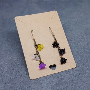 May include: A pair of dangle earrings with a chain and multiple flower charms. The flowers are in shades of purple, white, yellow, and black.